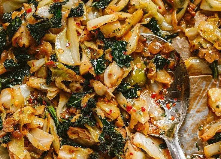 A skillet of garlic sautéed cabbage and kale, garnished with herbs.