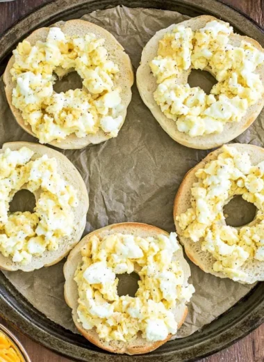 Breakfast pizza bagels topped with eggs, cheese, and vegetables.
