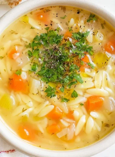 Bowl of hearty orzo soup with vegetables and herbs.