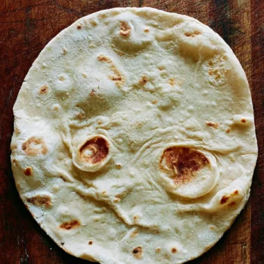 Homemade sourdough tortillas served on a wooden board with fresh ingredients.