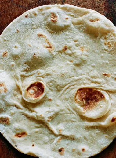 Homemade sourdough tortillas served on a wooden board with fresh ingredients.