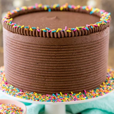 Moist yellow cake topped with creamy chocolate frosting on a white plate.