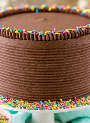Moist yellow cake topped with creamy chocolate frosting on a white plate.