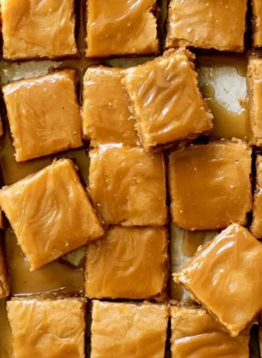 Cozy maple blondies drizzled with maple glaze on a wooden surface.
