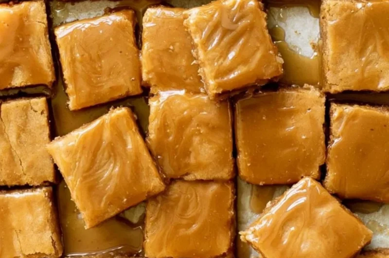 Cozy maple blondies drizzled with maple glaze on a wooden surface.